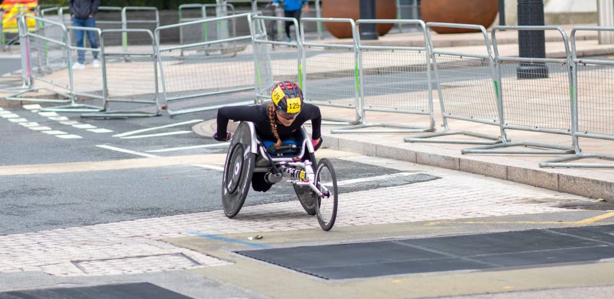 A dedicated athlete competes in a marathon using a racing wheelchair on city streets.